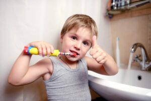Young boy brushing his teeth and making a thumbs up