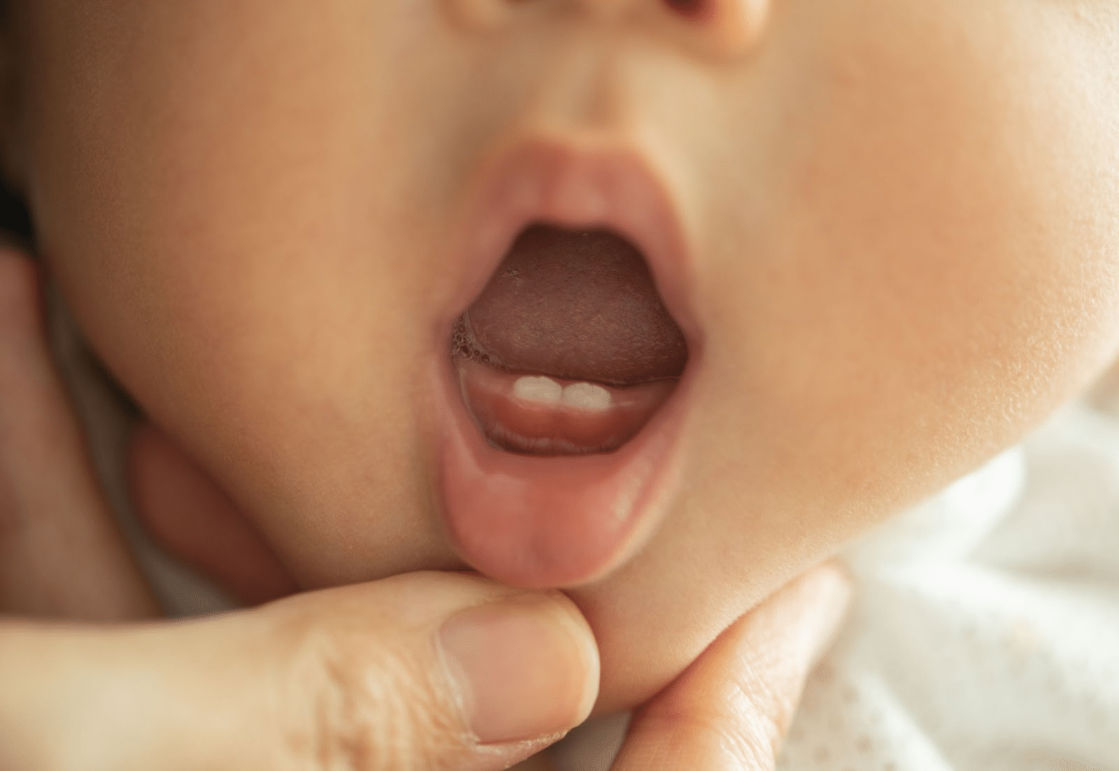 Adult gently revealing baby’s two healthy bottom teeth